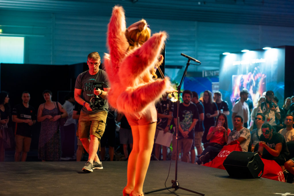 cameraman films a Popstar Ahri coslayer who is performing with a violin on stage infront of an audience.