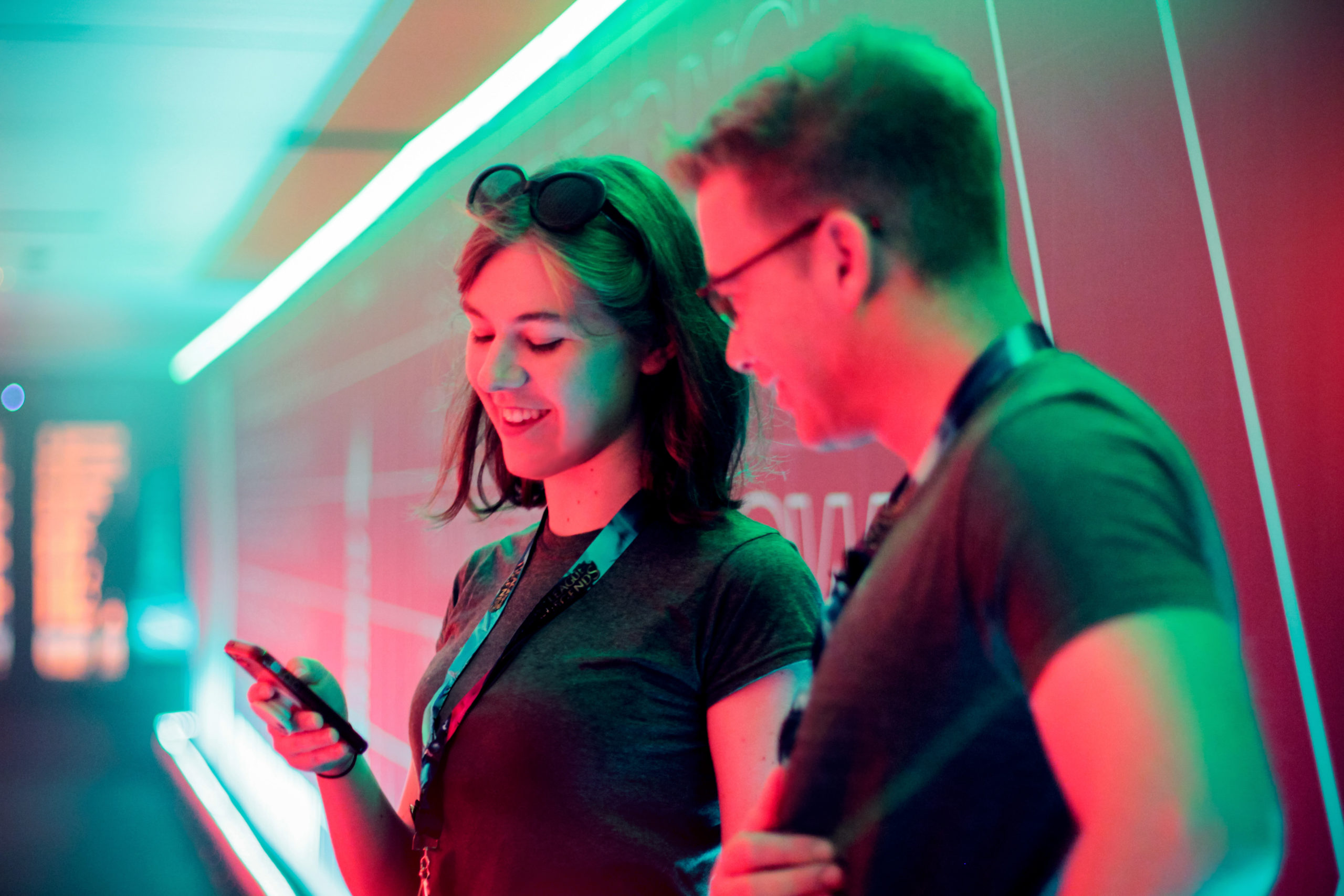 Girl laughs at something on her phone as she shows her co-worker in a red and teal light tunnel